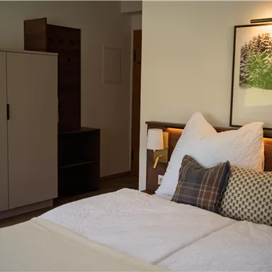 Ein modernes Schlafzimmer mit einem Doppelbett und stilvollen Kissen. Im Hintergrund befindet sich ein Kleiderschrank und ein Kunstwerk mit einer winterlichen Landschaft.
