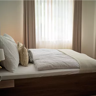 Ein gemütliches Schlafzimmer mit einem großen Bett und hellen Vorhängen. Die Einrichtung ist modern und einladend.