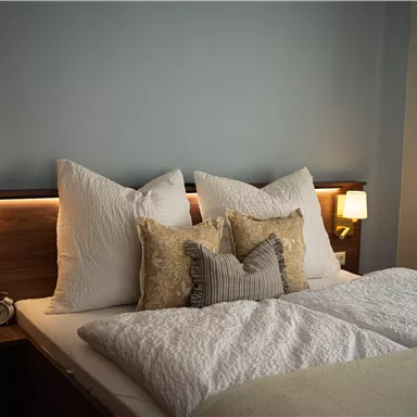 Ein gemütliches Schlafzimmer mit einem großen Bett. Der Raum ist in sanften Farben gehalten und hat zwei Nachtlichter an den Seiten.