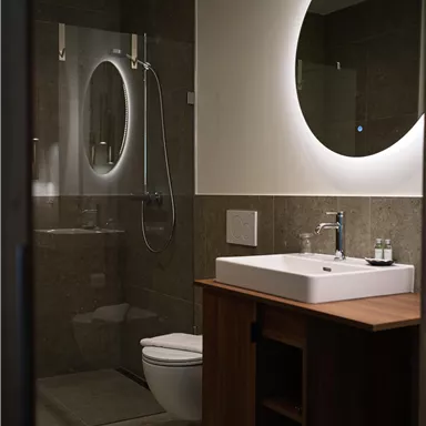 Ein modernes Badezimmer mit einer Dusche, einem Waschbecken und einem großen Spiegel. Die warmen Farbtöne und die minimalistische Einrichtung schaffen eine einladende Atmosphäre.