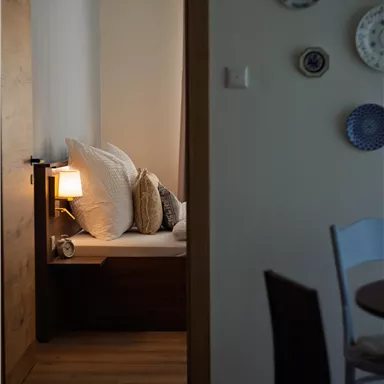 Ein gemütlicher Raum mit einem Bett, das mit großen Kissen ausgestattet ist. Im Hintergrund steht eine Lampe und dekorative Teller an der Wand.