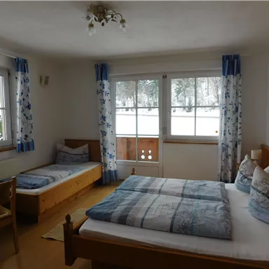 Ein gemütliches Zimmer mit zwei Betten und einem großen Fenster. Die Wände sind hell, und die Vorhänge sind blumig gestaltet.
