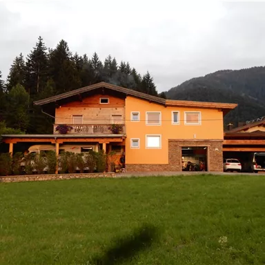 An orange house with a large garden and an adjacent garage. In the background, mountains and trees are visible.