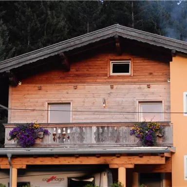 A cozy house with a wooden balcony and colorful flowers. In the background, there are tall, green trees.