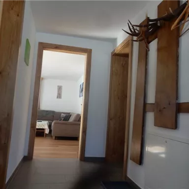 A bright hallway with wooden details and a window to the living room. On the left side, coat hooks are hanging on the wall.
