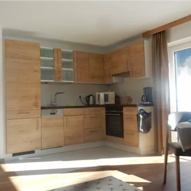 A modern kitchen with furniture made of light wood. It includes various appliances and a table with chairs.