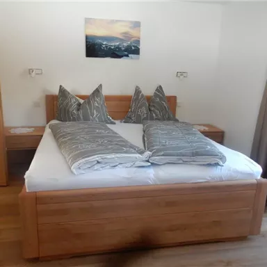 A cozy bedroom with a large double bed and stylish gray pillows. A picture of a mountain landscape hangs on the wall.
