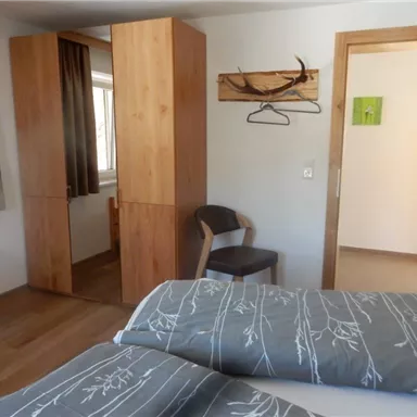 A cozy bedroom with wooden furniture and two beds. The walls are light, and there is a small desk as well as a chair.