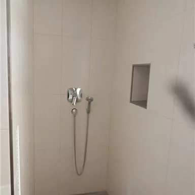 A modern shower with bright tiles and a rain shower. The wall has a small shelf.
