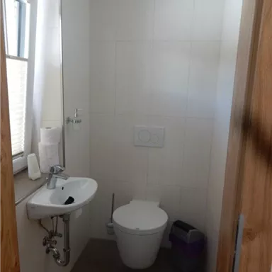 A small, modern bathroom with a toilet and a sink. It has light walls and a window that lets in daylight.