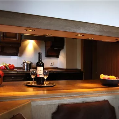 An elegant kitchen with wooden details and various foods. On the table are a bottle of wine and glasses, surrounded by fresh fruits.