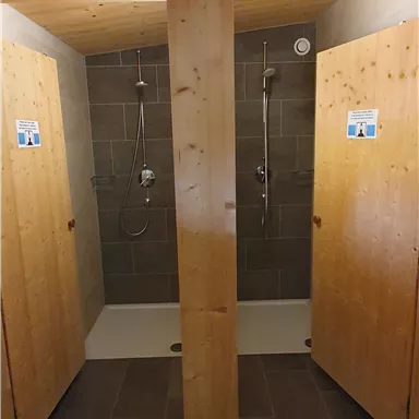 Two shower cabins with wood paneling and modern shower heads. The walls are tiled and the floor is laid with tiles.