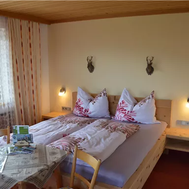 A cozy bedroom with two beds and rustic wood design. Next to the bed are a table and chairs, and the walls are adorned with decorative elements.