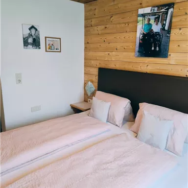 Ein gemütliches Schlafzimmer mit einem Doppelbett und hellen, weichen Bettdecken. An der Wand hängen einige Bilder, die eine warme Atmosphäre schaffen.