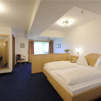 A cozy hotel room with a double bed and modern wooden decor. The room is bright and friendly, equipped with a table, a chair, and a mirror.