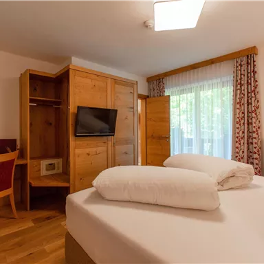 A cozy hotel room with a double bed, a desk, and a television. Large windows provide plenty of natural light.
