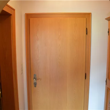 A bright hallway with a wooden door and a wardrobe. On the left side, access to a bathroom is visible.