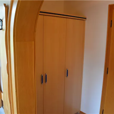 A simple room with a wooden wardrobe and an open shelf. Several coat hooks are hanging on the wall.