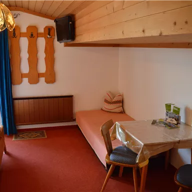 A cozy room with wooden details and a comfortable single bed. There are two chairs at the table and an information booklet.