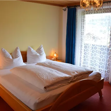 A cozy bedroom with a double bed and two large pillows. The room has a bright atmosphere and a window with curtains.