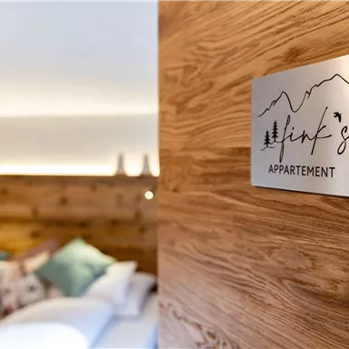 A modern apartment with a wooden sign that says "Link's Apartment." In the background, cozy cushions and warm lighting are visible.