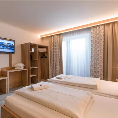 A modern hotel room with two beds and a television. Large windows let in plenty of daylight and create a bright atmosphere.