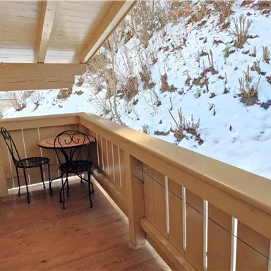 A small balcony with a table and two chairs. In the background, there is snow and a grassy area.