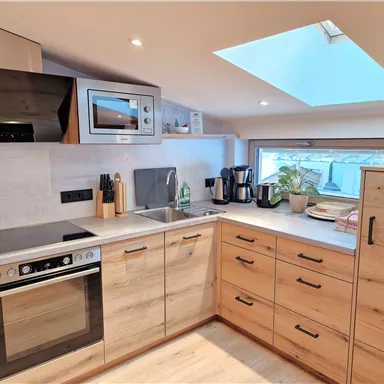 A modern kitchen with wooden cabinets and appliances. A window with a skylight provides plenty of light.