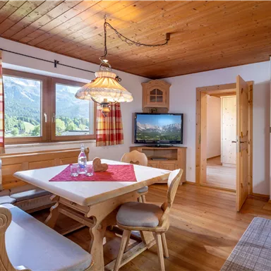 A cozy kitchen with a wooden table and chairs. The windows offer a view of the mountains, and there is a television in the corner.