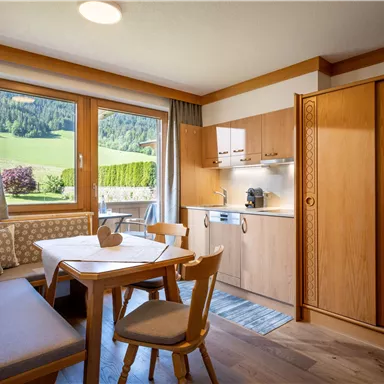 A cozy living room with wooden furniture and a table. Through the window, one can see a green landscape with mountains.