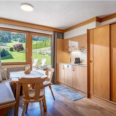A cozy holiday apartment with wooden interiors and a beautiful view of the green landscape. The space offers a small kitchen and a dining area with a table and chairs.