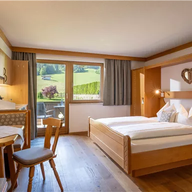 A cozy room with a double bed and wooden furniture. Through the window, one looks out at a green landscape.