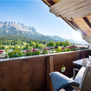 A beautiful balcony with a view of the mountains and a green landscape. Sunshine and flowers give the scene an inviting atmosphere.
