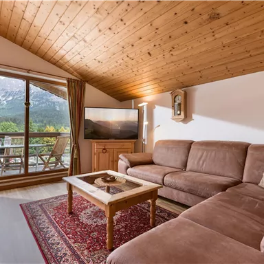 Ein gemütliches Wohnzimmer mit einem großen Fenster, das einen Blick auf die Berge bietet. Der Raum ist mit einem beigen Sofa und einem Holztisch ausgestattet.