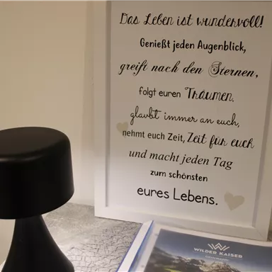 A stylish black with a round lamp and a framed quote about life. Below it lies a brochure with a beautiful landscape.