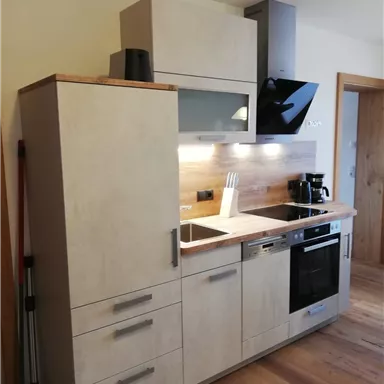 Eine moderne Küche mit einer klaren, minimalistischen Gestaltung. Sie verfügt über Holz- und graue Schrankelemente sowie moderne Geräte.