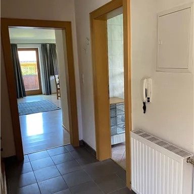 A bright hallway with two open doors and a tiled floor. On the right side, there is a radiator.