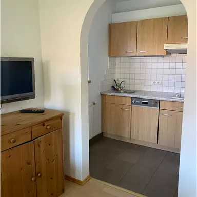 A modern kitchen with wooden cabinets and a large refrigerator. The entrance is marked by a round arch.