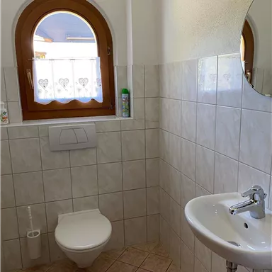 A bathroom with ceramic tiles and an oval window. There is a toilet and a hand basin.