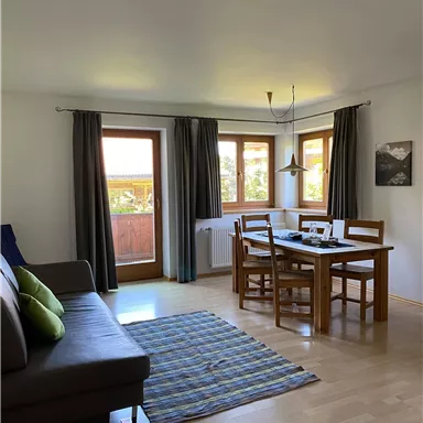 A cozy living space with a dining table and a couch. Large windows provide plenty of daylight and a view outside.