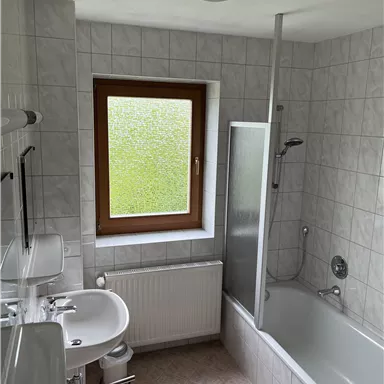 A modern bathroom with a bathtub and a shower. A window provides daylight and fresh air.
