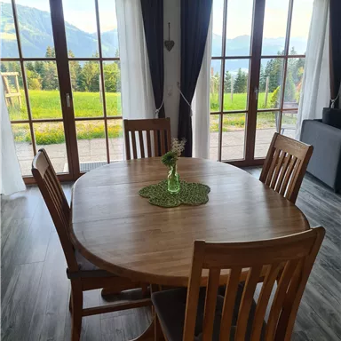 Ein einladender Essbereich mit einem runden Holztisch und Stühlen. Große Fenster bieten einen Blick auf die umliegende Landschaft.