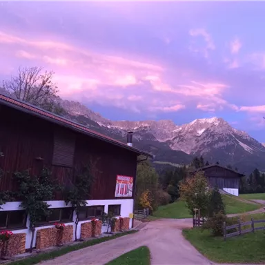 A picturesque landscape with mountains in the background and a beautiful evening sky. In the foreground, there are wood piles and rural buildings.