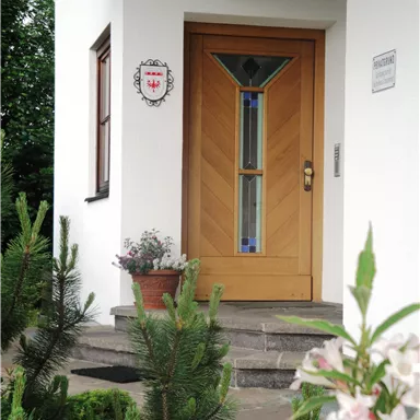 A cozy wooden front door with a colorful glass element. In the foreground, there are green plants and flowers.