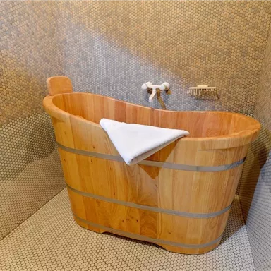 Eine stilvolle Holzbadewanne steht in einem modern gefliesten Badezimmer. Die Wände sind mit kleinen, runden Fliesen in neutralen Farben dekoriert.