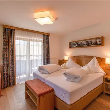 A modern bedroom with wooden details and a double bed. The room features a balcony and a cozy seating area.