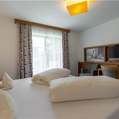 A cozy hotel room with a large bed and modern furniture. There are windows that let in plenty of daylight, as well as a television and a workspace.