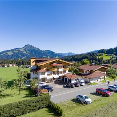 A picturesque hotel in a rural setting with green meadows and mountains in the background. The weather is nice and clear, perfect for a stay in nature.