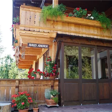 A traditional wooden house with a balcony decorated with flowers. The entrance area is inviting and friendly designed.