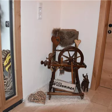 A traditional spinning wheel and a welcome sign are located in a cozy corner. The surroundings are made of wood and feature a rustic charm.